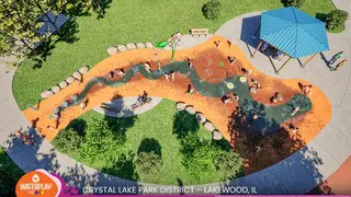 Aerial view of a splash pad design with an orange, winding path resembling a river, surrounded by green grass and a blue shaded structure. The text at the bottom reads "WATERPLAY CRYSTAL LAKE PARK DISTRICT - LAKEWOOD, IL".