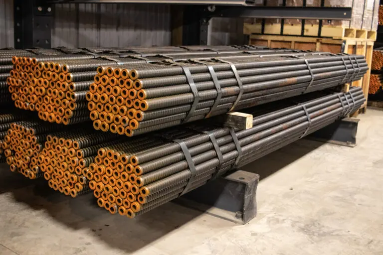 Bundles of Magnacore R38 Anchor Hollow Bars, showing the threaded steel rods with orange-capped ends, stacked in a warehouse.