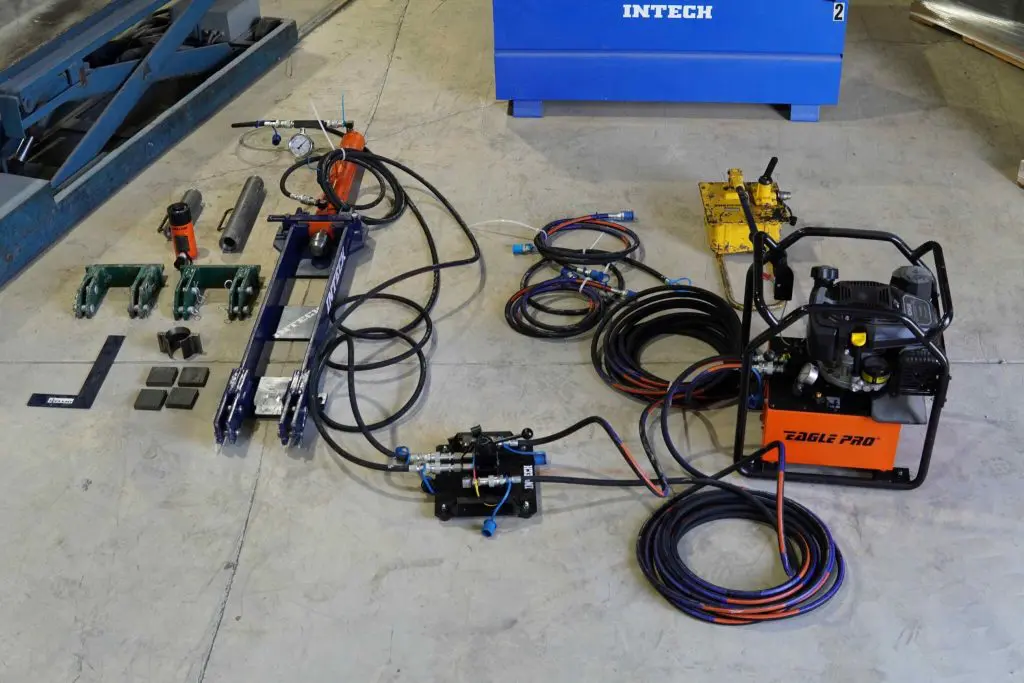 A collection of hydraulic resistance equipment, including a power unit labeled 'EAGLE PRO', hoses, a control valve, and various blue and green metal components, laid out on a concrete floor.