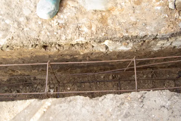 A construction trench with exposed earth, showing a cage of steel rebar (reinforcement bar) for a concrete foundation or shoring.