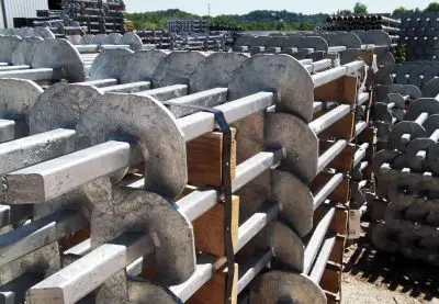 Galvanized steel helical piles with square shafts and circular helix plates stacked on wooden pallets in a storage yard.