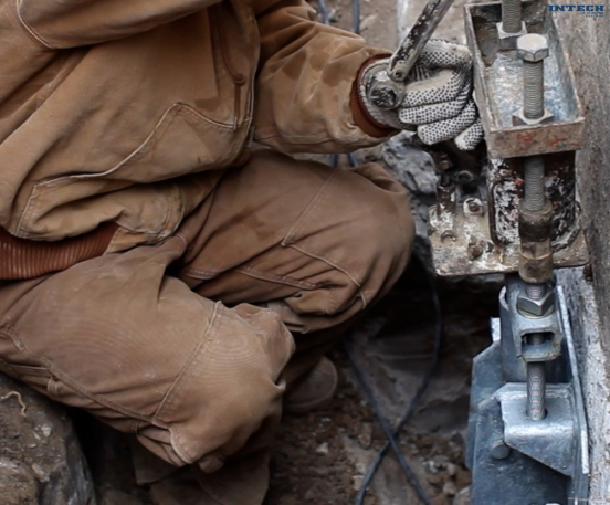 Close-up of a worker in brown workwear operating a hydraulic jack or structural stabilization equipment on a foundation.